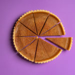 A chocolate pie against a purple background. The pie has been cut into 10 slices, with one being removed