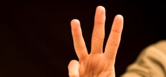 Photo of a hand holding up three fingers.