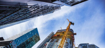 Low angle view of concrete and steel skyscrapers in blue glass with cranes around