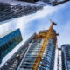 Low angle view of concrete and steel skyscrapers in blue glass with cranes around